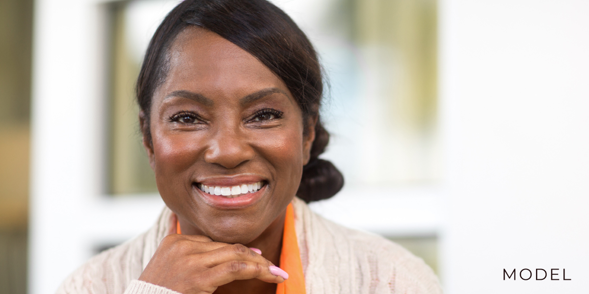 Model Smiles Directly at Camera While Resting Head on Back of Her Right Hand