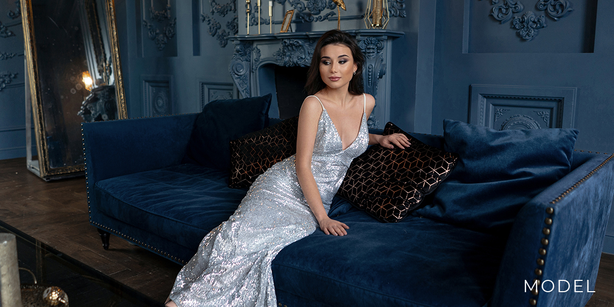 Model in silver dress leans on a couch | emmett plastic surgery