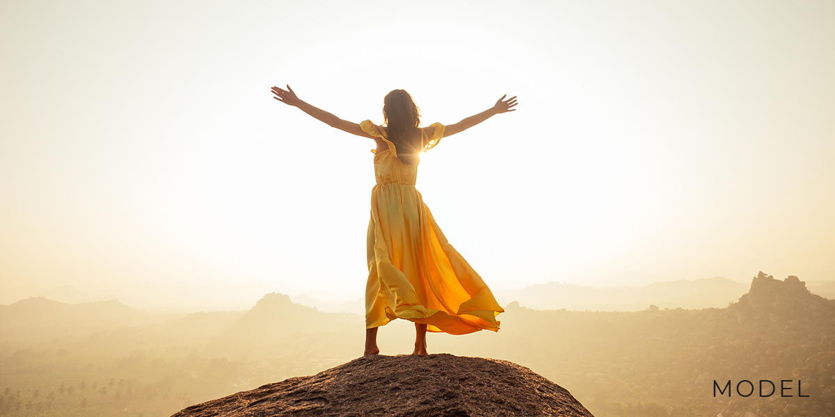Woman Stands in Front of the Sunset with Arms Outstretched
